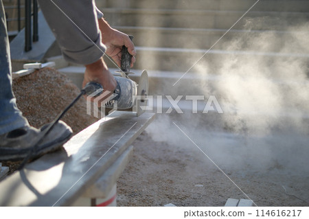 A man is using a grinder to cut a piece of concrete 114616217