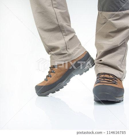 Trekking boots for hiking on the legs of a tourist on a white background. Trekking boots for hiking on the legs of a tourist on a white background. 114616785