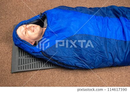 man sleeps in a sleeping bag. items for tourism and camping man sleeps in a sleeping bag. items for tourism and camping 114617390