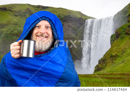bearded man in a sleeping bag with a cup of coffee against the backdrop of nature in the mountains bearded man in a sleeping bag with a cup of coffee against the backdrop of nature in the mountains 114617484