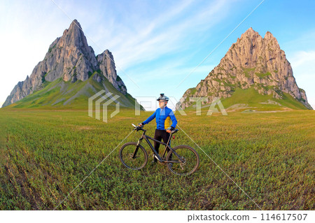 cyclist with bicycle is resting on a green field against a blue sky. sports and recreation in nature cyclist with bicycle is resting on a green field against a blue sky. sports and recreation in nature 114617507