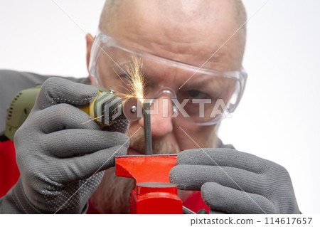 Bearded man mechanic processes metal with an engraving drill. Locksmith industry. Bearded man mechanic processes metal with an engraving drill. Locksmith industry. 114617657