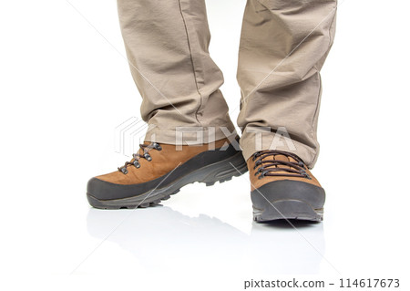 Trekking boots for hiking on the legs of a tourist on a white background. Trekking boots for hiking on the legs of a tourist on a white background. 114617673