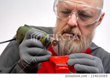 Bearded man mechanic processes metal with an engraving drill. Locksmith industry. Bearded man mechanic processes metal with an engraving drill. Locksmith industry. 114618369