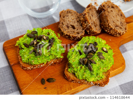 Multigrain toasts with guacamole and pumpkin seeds on wooden board 114618644