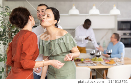Asian woman greetingly kissing female friend at dinner party Asian woman greetingly kissing female friend at dinner party 114618761