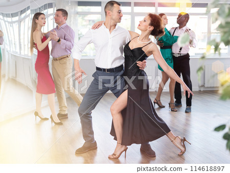 Dance training in group - men and women of different nationalities and different ages dance tango or bachata in dance studio Dance training in group - men and women of different nationalities and different ages dance tango or bachata in dance studio 114618897