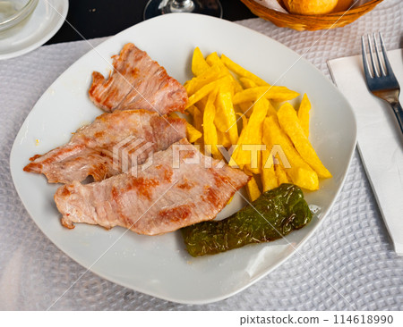 Appetizing grilled pork escalope with side dish of fried potatoes and baked pepper served at plate. Spanish cuisine Secreto de cerdo 114618990