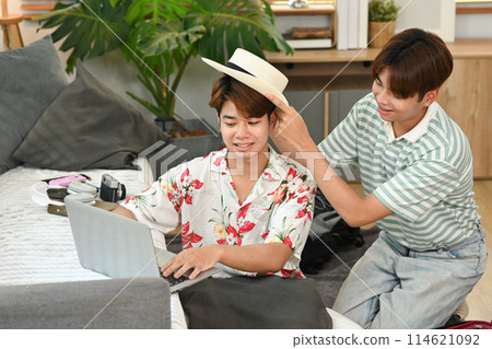 Young male lovers packing suitcase and booking hotel reservation via laptop at home Young male lovers packing suitcase and booking hotel reservation via laptop at home 114621092