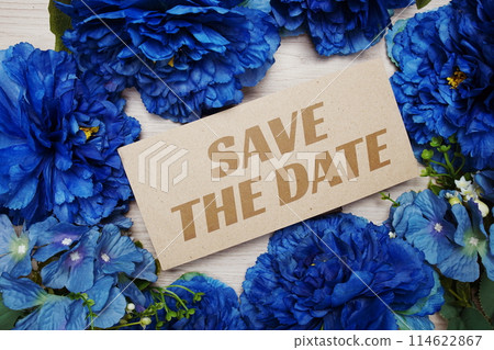 Save the Date text message on paper card with flowers border frame on wooden background 114622867