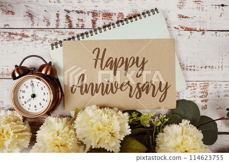 Happy Anniversary text message on paper card with flowers border frame on wooden background Happy Anniversary text message on paper card with flowers border frame on wooden background 114623755