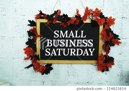 Small Business Saturday text message on Blackboard decoration with maple leaves hanging on a concrete wall background Small Business Saturday text message on Blackboard decoration with maple leaves hanging on a concrete wall background 114623814