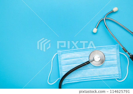 Stethoscope and medical disposable mask for protection against viruses on a blue background. Stethoscope and medical disposable mask for protection against viruses on a blue background. 114625791