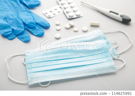 Medical thermometer and mask with pills on grey. Medical concept with copy space Medical thermometer and mask with pills on grey. Medical concept with copy space 114625991