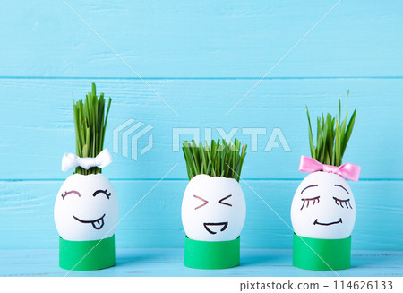 Cute handmade eggs with hair of green grass with copy space. Easter concept on blue background 114626133