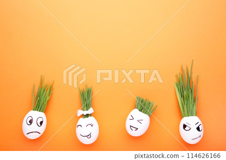 Cute handmade eggs with hair of green grass with copy space. Easter concept on orange background Cute handmade eggs with hair of green grass with copy space. Easter concept on orange background 114626166