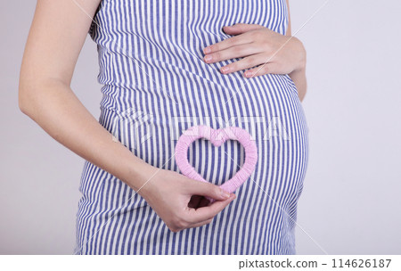 Pregnant women holding heart symbol placed on belly on grey background 114626187