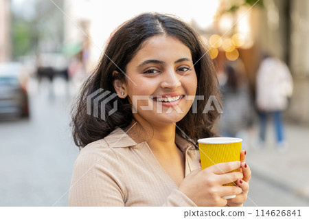 Happy Indian woman enjoying drinking morning coffee hot drink relaxing taking a break on city street 114626841