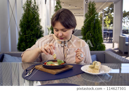 medium sized woman in peach fuzz dress eating Shakshouka in modern restaurant medium sized woman in peach fuzz dress eating Shakshouka in modern restaurant 114627301