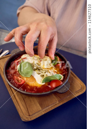 medium sized woman in peach fuzz dress eating Shakshouka in modern restaurant medium sized woman in peach fuzz dress eating Shakshouka in modern restaurant 114627310