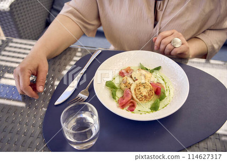 a medium sized woman in peach fuzz dress eating cottage cheese pancakes with salmon and spinach in modern restaurant a medium sized woman in peach fuzz dress eating cottage cheese pancakes with salmon and spinach in modern restaurant 114627317