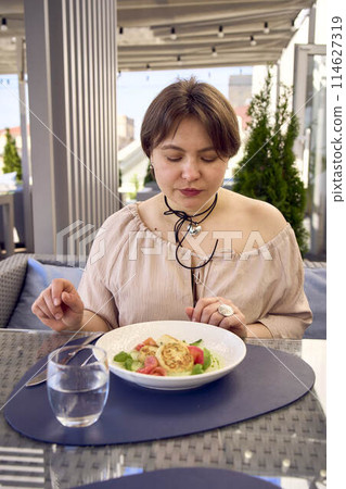 medium sized woman in peach fuzz dress eating cottage cheese pancakes with salmon and spinach in modern restaurant medium sized woman in peach fuzz dress eating cottage cheese pancakes with salmon and spinach in modern restaurant 114627319