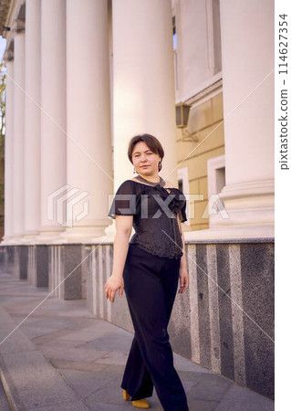 a medium-sized woman in a black corset near a theater with antique columns 114627354