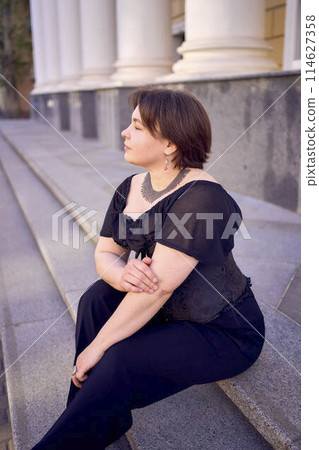 a medium-sized woman in a black corset near a theater with antique columns a medium-sized woman in a black corset near a theater with antique columns 114627358