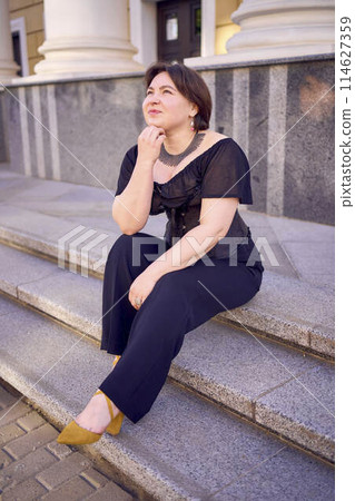 a medium-sized woman in a black corset near a theater with antique columns 114627359