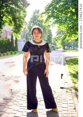 a    medium size woman in a black corset and wide leg trousers walks through the city in the morning light 114627410