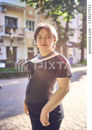 a    medium size woman in a black corset and wide leg trousers walks through the city in the morning light 114627411
