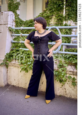 a medium size woman in a black corset and wide leg trousers walks through the city in the morning light a medium size woman in a black corset and wide leg trousers walks through the city in the morning light 114627428