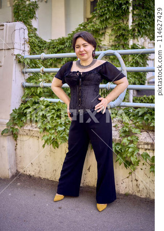 a medium size woman in a black corset and wide leg trousers walks through the city in the morning light a medium size woman in a black corset and wide leg trousers walks through the city in the morning light 114627429