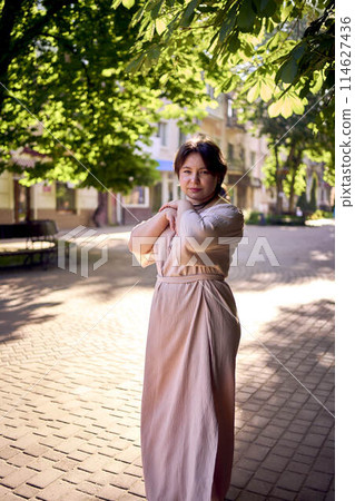 plus size woman in a peach fuzz dress walks through the morning city 114627436