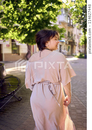 plus size woman in peach fuzz dress dancing on the streets of the morning city 114627448
