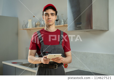 Professional Repairman in Red Uniform Using Tablet in Modern Kitchen During Daytime 114627521