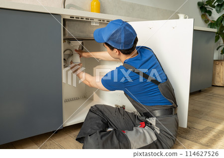 Professional Plumber Repairs Under-Sink Pipes in a Modern Kitchen Professional Plumber Repairs Under-Sink Pipes in a Modern Kitchen 114627526
