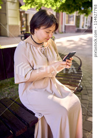 a plus size woman in peach fuzz dress talking on phone in morning city 114627768