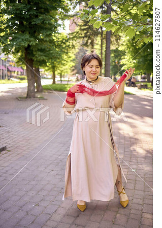 plus size woman in peach fuzz dress and red translucent gloves dancing in the morning city streets 114627807