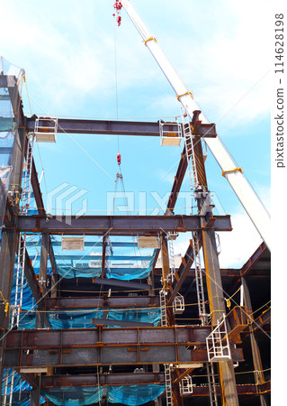 A crane working on steel frames during a building construction project A crane working on steel frames during a building construction project 114628198