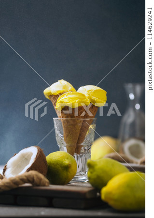 Lemon yellow ice cream in a waffle horn on a dark blue and wooden background. coconut and fruit ice cream. Promotional photo in a dark mood. food photography Lemon yellow ice cream in a waffle horn on a dark blue and wooden background. coconut and fruit ice cream. Promotional photo in a dark mood. food photography 114629241