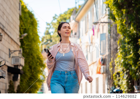 Portrait of happy pretty young Caucasian woman walks through an old Mediterranean city with an online guide on her smartphone. Summer vacation Portrait of happy pretty young Caucasian woman walks through an old Mediterranean city with an online guide on her smartphone. Summer vacation 114629882