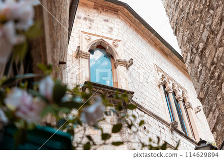 Beautiful window in Gothic building with sky reflection. Bottom view of monastery building in old Mediterranean city. Concept of religion and hope Beautiful window in Gothic building with sky reflection. Bottom view of monastery building in old Mediterranean city. Concept of religion and hope 114629894
