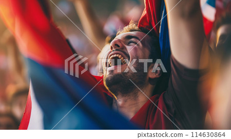 a soccer fan, their eyes shining with passion as they raise their scarf high in the air 114630864
