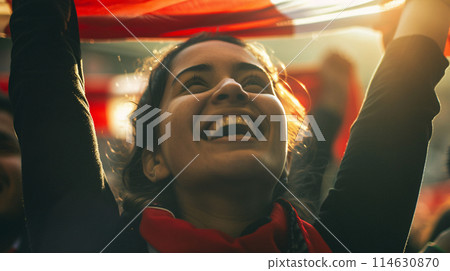 a soccer fan, their eyes shining with passion as they raise their scarf high in the air 114630870