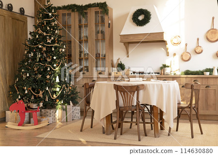 kitchen decorated with pine garlands and Christmas toys. the table and near is worth Christmas tree. interior bright kitchen decorated for Christmas kitchen decorated with pine garlands and Christmas toys. the table and near is worth Christmas tree. interior bright kitchen decorated for Christmas 114630880