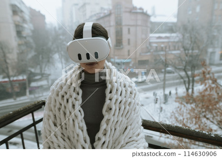 Winter vistas surround a girl experiencing VR on the balcony with a headset. 114630906