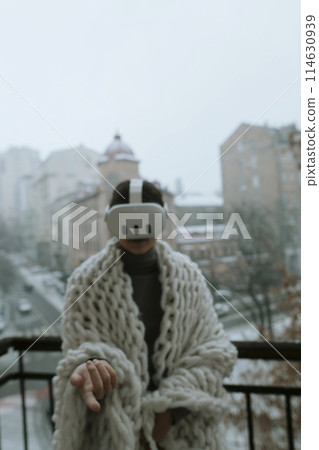 A young woman in a virtual reality headset stands on the balcony in winter. A young woman in a virtual reality headset stands on the balcony in winter. 114630939