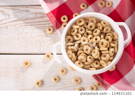 healthy cereal rings on a light wood background with tablecloth red in a plate and scattered on the table with sun rays. morning eat. Healthy children's breakfast. Dry muesli. 114631101