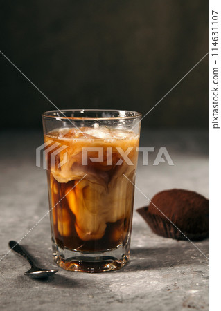 Iced coffee in a tall glass topped with cream and chocolate chip cookies on a gray rustic table. Cold summer drink on a dark background. 114631107
